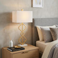 32" White Geometric Table Lamp With Shade displayed on a dark wood tabletop in a furnished interior against a cream wall.