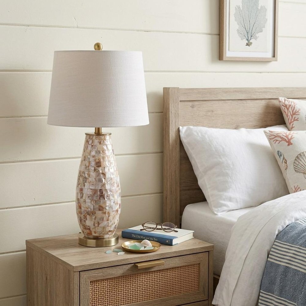 28" Gold Novelty Table Lamp With Drum Shade displayed on a dark wood tabletop in a furnished interior against an off-white wall.