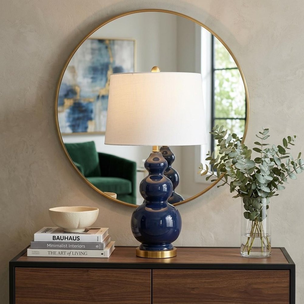 28" Navy Blue And Gold Novelty Table Lamp With Empire Shade displayed on a dark wood tabletop in a furnished interior against a tan wall.