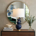 28" Navy Blue And Gold Novelty Table Lamp With Empire Shade displayed on a dark wood tabletop in a furnished interior against a tan wall.