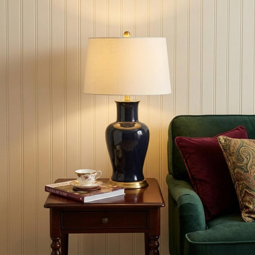 29" Navy Blue And Gold Urn Bedside Lamp With Drum Shade styled in a furnished interior with a cream wall on a black floor.