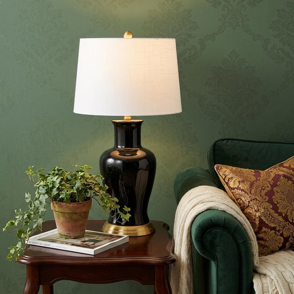 29" Gold Urn Table Lamp With Drum Shade shown outdoors on an outdoor setting with greenery.