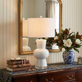 29" Clear Novelty Table Lamp With Drum Shade displayed on a tabletop in a furnished interior against a cream wall.