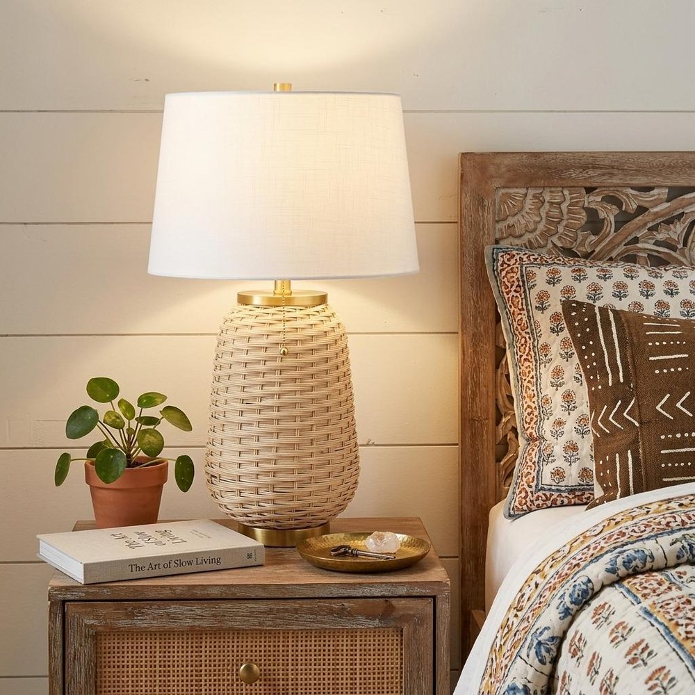 25" Gold Urn Table Lamp With Empire Shade displayed on a dark wood tabletop in a furnished interior against a cream wall.