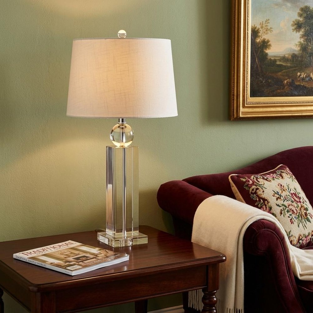 29" Silver And Clear Table Lamp With Empire Shade displayed on a tabletop in a furnished interior against a tan wall.