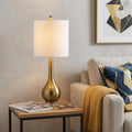 25" Clear Gourd Table Lamp With Drum Shade displayed on a dark wood tabletop in a furnished interior against a light gray wall.