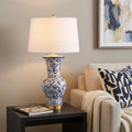 29" Gold Novelty Table Lamp With Drum Shade displayed on a tabletop in a furnished interior against a tan wall.