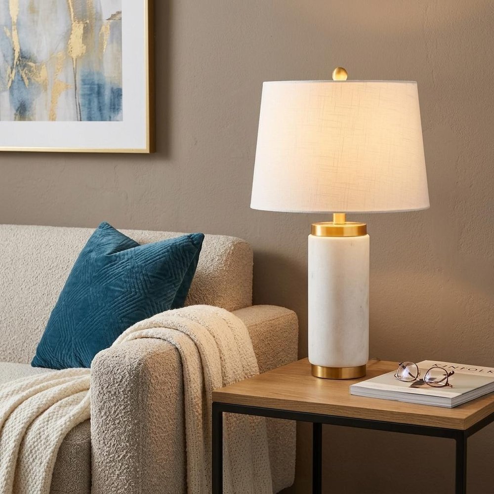23" White And Gold Bedside Lamp With Empire Shade styled in a furnished interior with a tan wall on a dark wood floor.