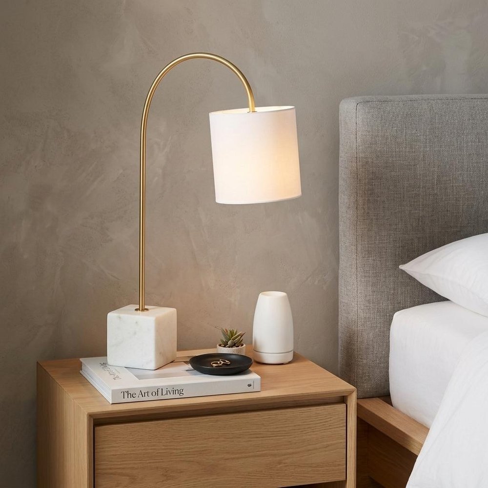 25" White Novelty Table Lamp With Drum Shade displayed on a dark wood tabletop in a furnished interior against a tan wall.