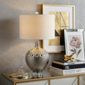 27" Clear Novelty Bedside Lamp With Drum Shade styled in a furnished interior with a tan wall on a tiled floor.