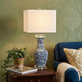 28" Clear Novelty Table Lamp With Square Shade displayed on a tabletop in a furnished interior against a gold wall.