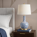 30" Blue White And Gold Gourd Table Lamp With Drum Shade displayed on a tabletop in a furnished interior against a tan wall.