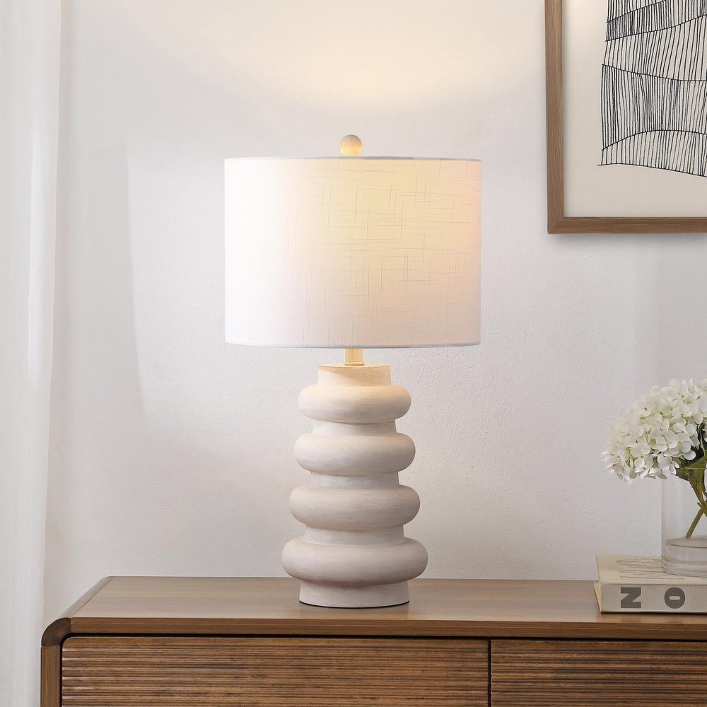 26" Clear Round Table Lamp With Drum Shade displayed on a dark wood tabletop in a furnished interior against an off-white wall.
