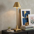 26" Gold Novelty Table Lamp With Drum Shade displayed on a tabletop in a furnished interior against a light gray wall.