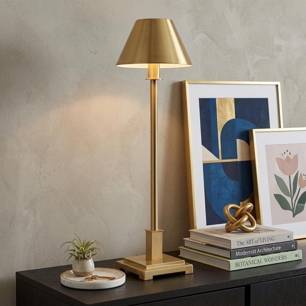 26" Gold Novelty Table Lamp With Drum Shade displayed on a tabletop in a furnished interior against a light gray wall.