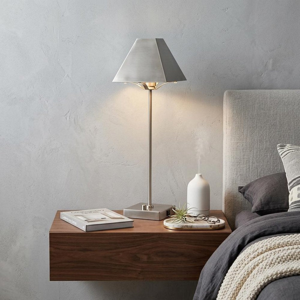 25" Nickel Table Lamp With Novelty Shade displayed on a dark wood tabletop in a furnished interior against a light gray wall in silver.