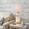 28" Gold Novelty Table Lamp With Shade displayed on a wood tabletop in a furnished interior against a light gray wall.