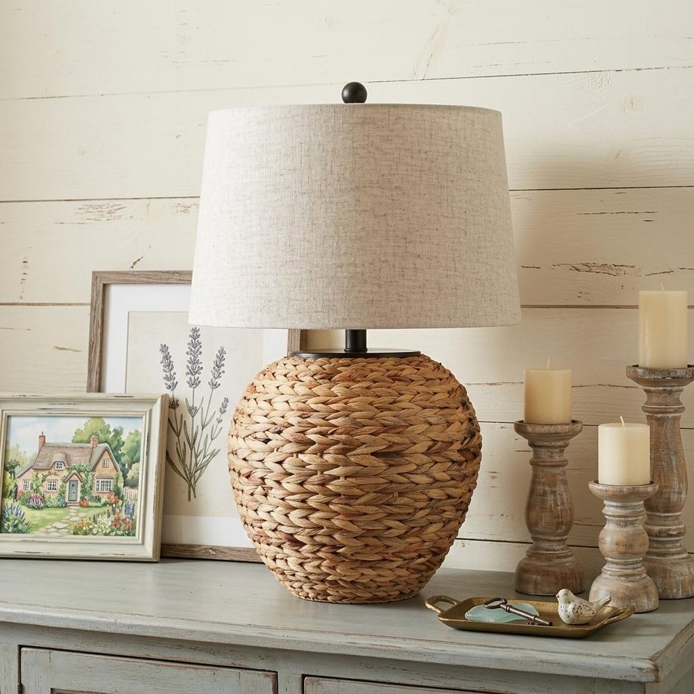 25" Clear Urn Table Lamp With Globe Shade displayed on a tabletop in a furnished interior against an off-white wall.