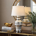 29" Silver Urn Table Lamp With Empire Shade displayed on a tabletop in a furnished interior against a tan wall.