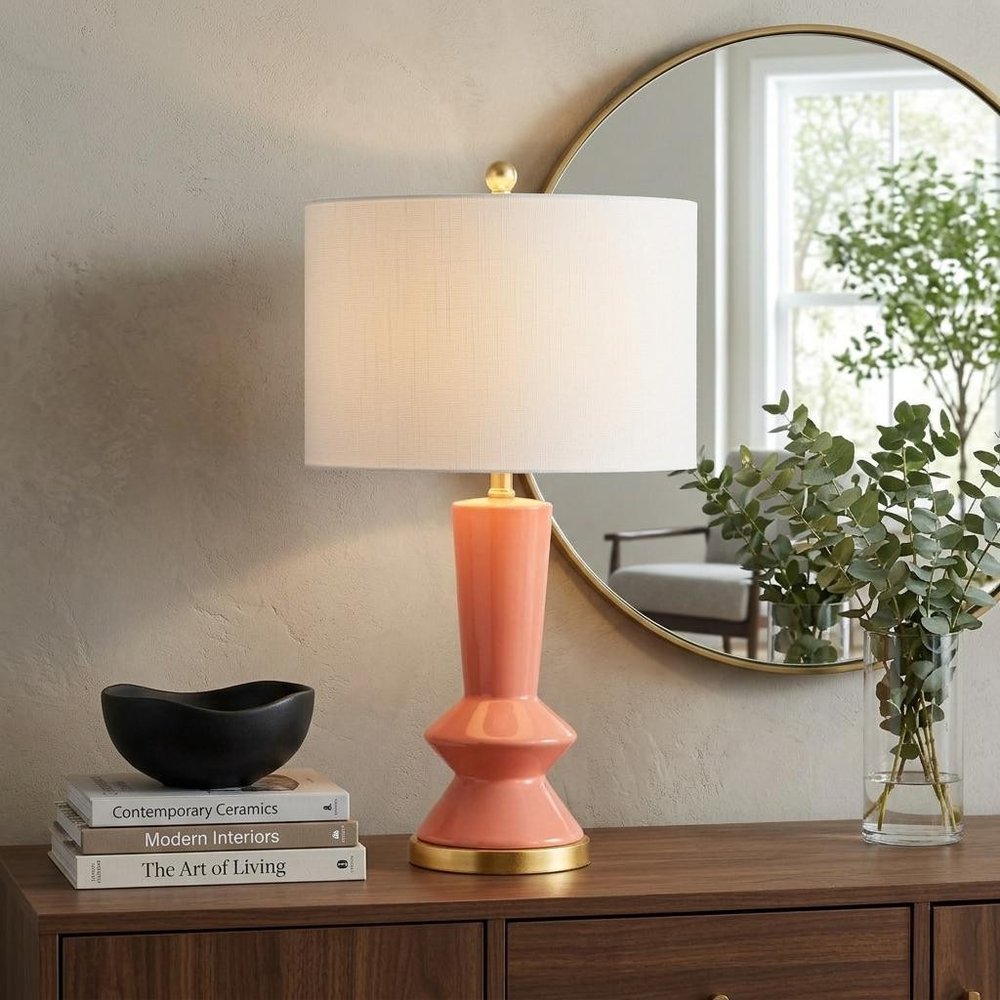 27" Gold Geometric Table Lamp With Drum Shade displayed on a dark wood tabletop in a furnished interior against a tan wall.