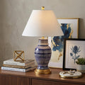 27" Navy Blue Gold And White Urn Table Lamp With Empire Shade displayed on a dark wood tabletop in a furnished interior against a tan wall.