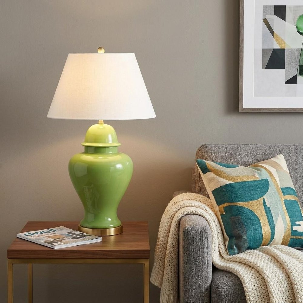 33" Green And Gold Urn Table Lamp With Empire Shade displayed on a dark wood tabletop in a furnished interior against a tan wall.