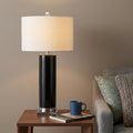 32" Silver Table Lamp With Drum Shade displayed on a dark wood tabletop in a furnished interior against a tan wall.