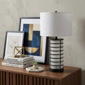 27" Black USB Table Lamp With Drum Shade displayed on a dark wood tabletop in a furnished interior against a light gray wall.