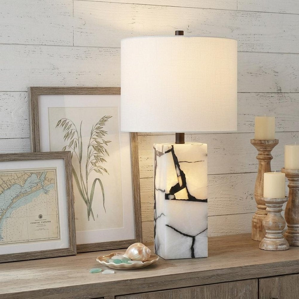 24" Black And White Table Lamp With Drum Shade displayed on a dark wood tabletop in a furnished interior against a light gray wall.