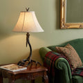 28" Black Antlers Table Lamp With Bell Shade displayed on a tabletop in a furnished interior against a tan wall.