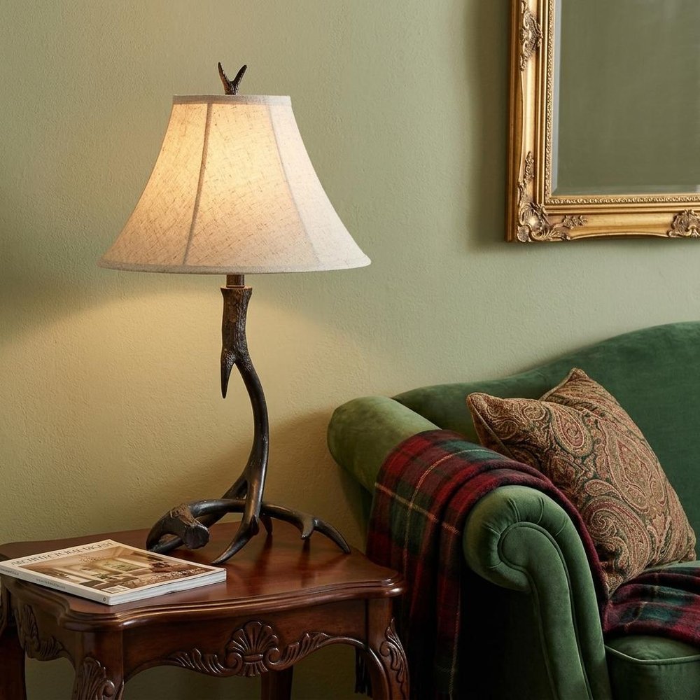28" Black Antlers Table Lamp With Bell Shade displayed on a tabletop in a furnished interior against a tan wall.