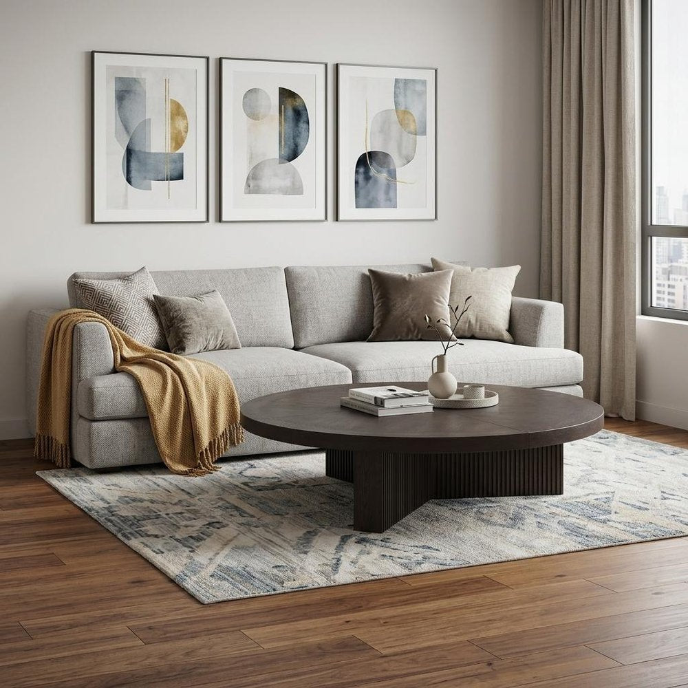 60" Espresso Wood Round Pedestal Coffee Table styled in a furnished interior with a light gray wall on a dark wood floor in light gray wood.