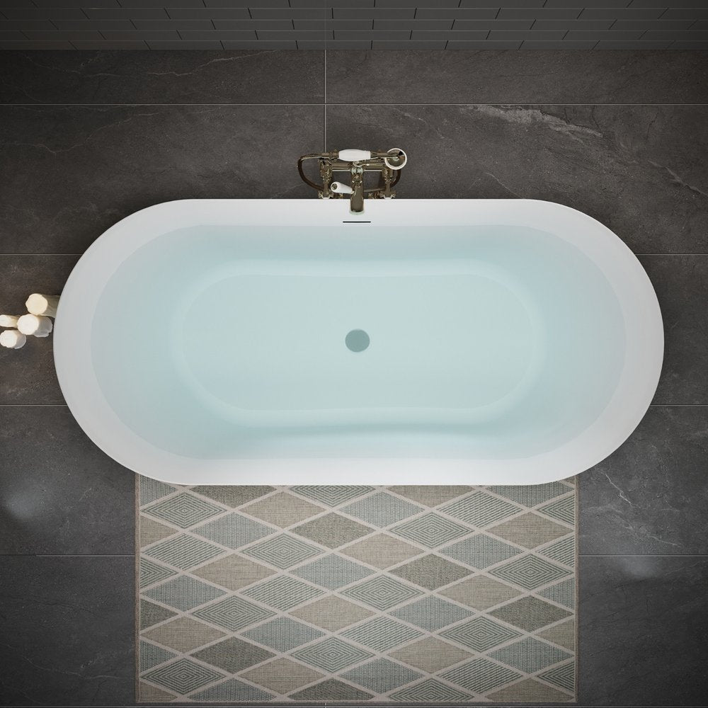 White acrylic oval bathtub filled with water on a dark tiled floor with a diamond pattern rug.