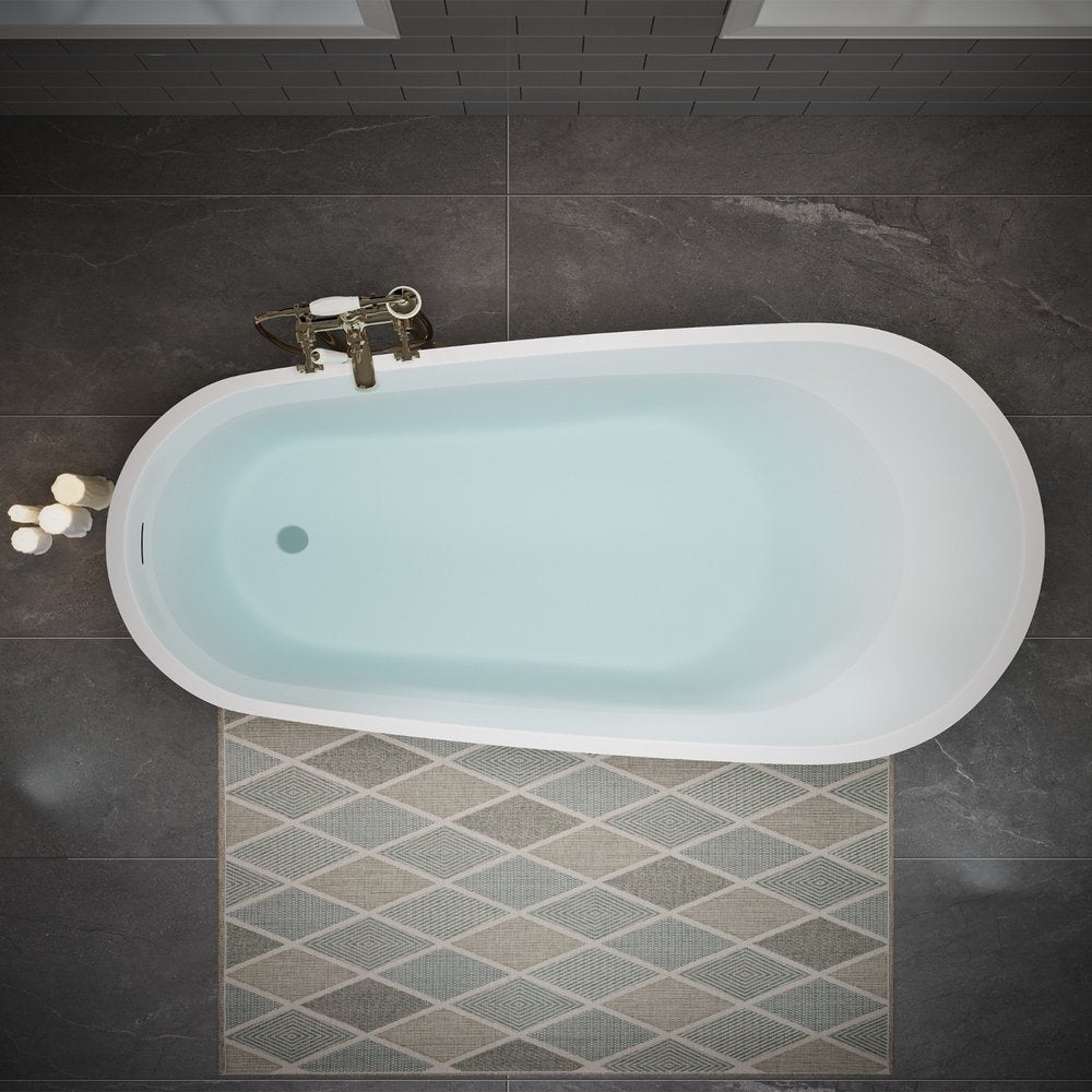 White acrylic oval bathtub filled with water, with brass faucet and bath mat on dark tile floor.