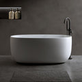 White acrylic oval freestanding bathtub with a black faucet and dark gray wall and floor.