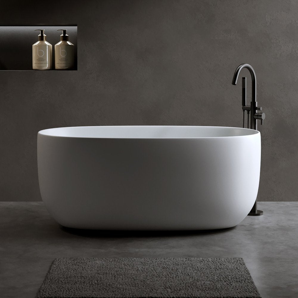 White acrylic oval freestanding bathtub with a black faucet and dark gray wall and floor.