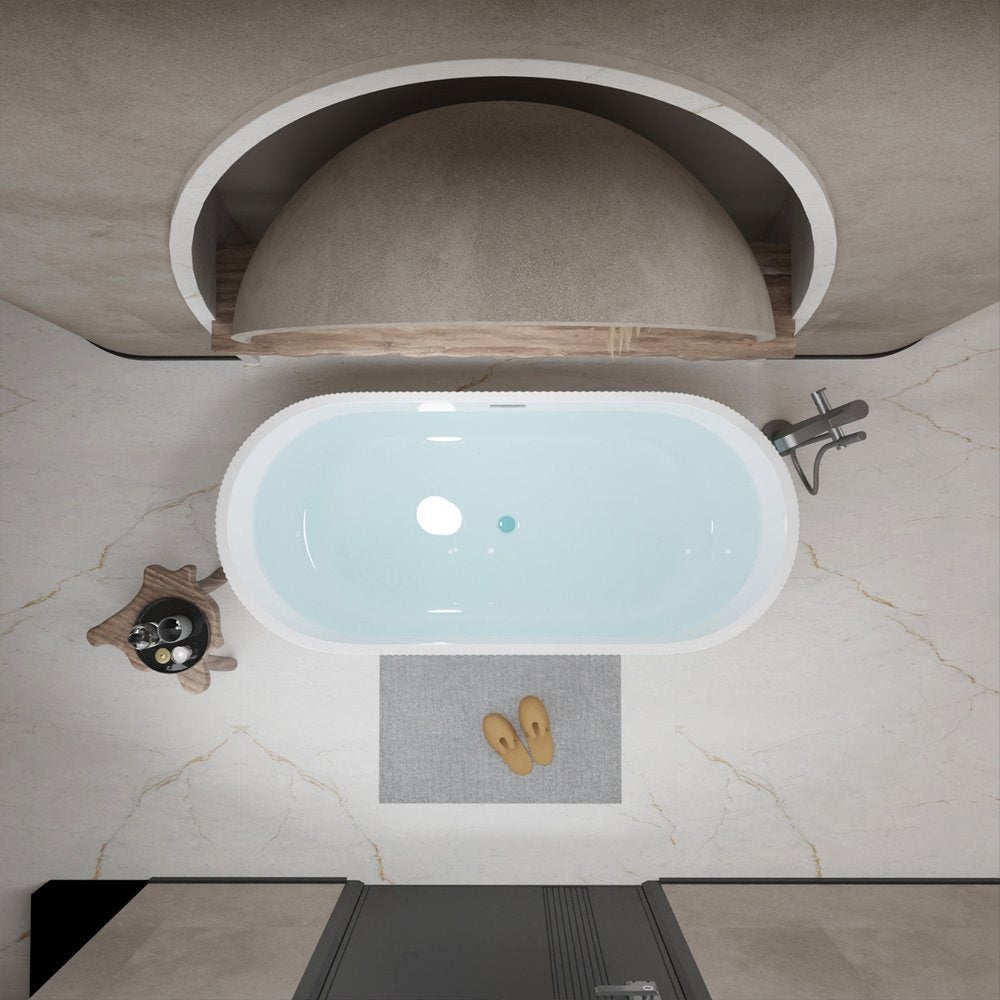 Top view of a white oval acrylic bathtub filled with water, with a grey mat and slippers on a marble floor.