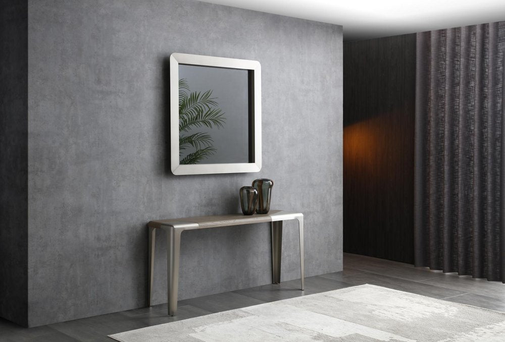 A light gray and nickel console table with a wood top and stainless steel legs stands against a gray wall with a mirror and two vases.