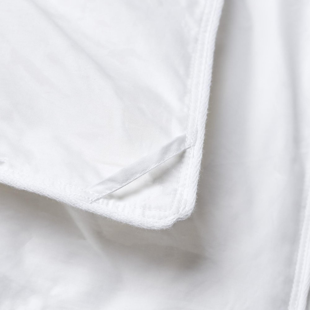 Close-up of a white cotton washable microfiber down alternative comforter showing a corner with a white ribbon tie.