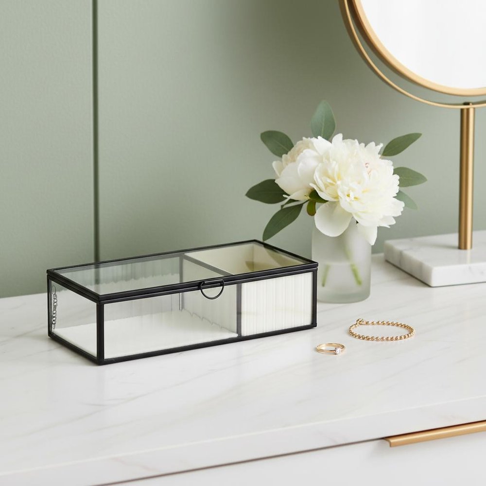 10" Black Glass Two Section Jewelry Box With Metal Accents styled in a furnished interior with a light gray wall on a off-white floor.