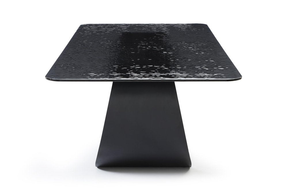 Black glass dining table with a textured surface and a matte black geometric pedestal base on a white background.