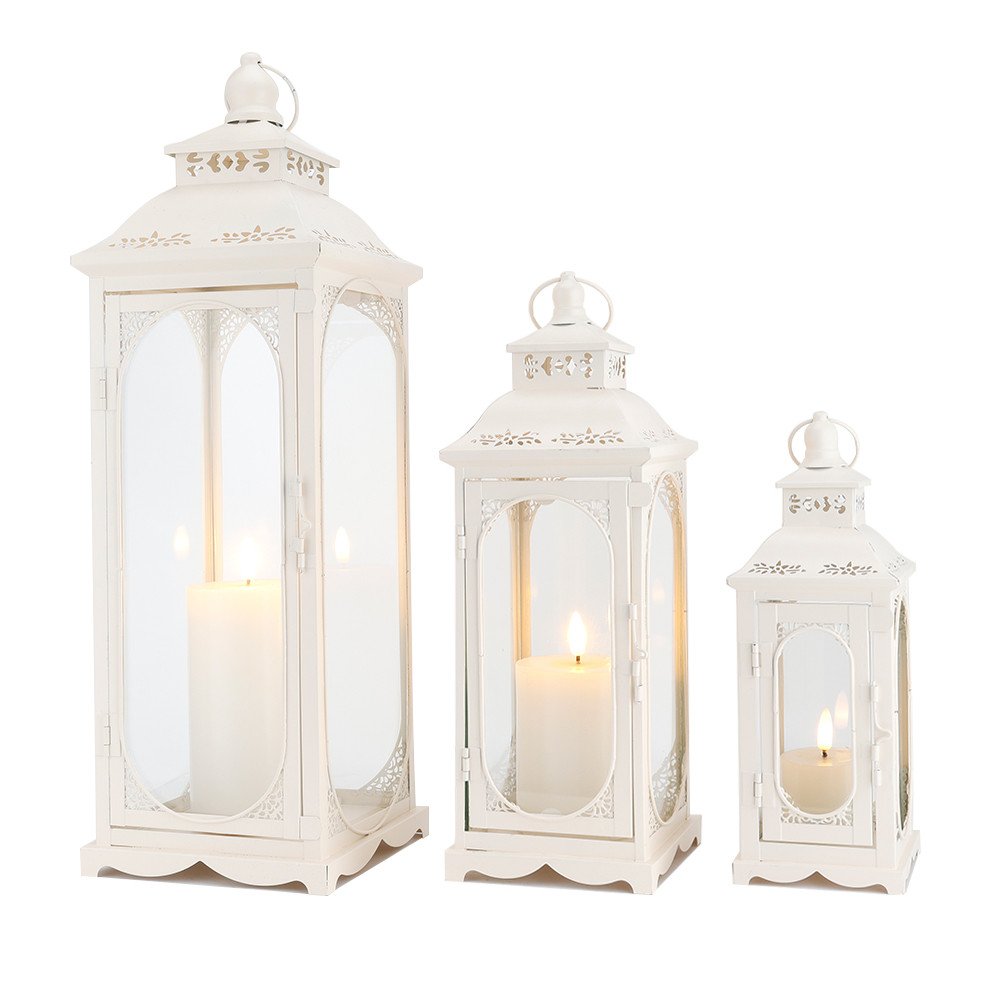 Three white metal and glass lanterns of varying sizes, each holding a lit candle, on a white background.