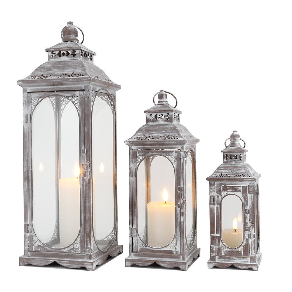 Three clear and gray metal tabletop lanterns with glass panels and lit candles on a white background.