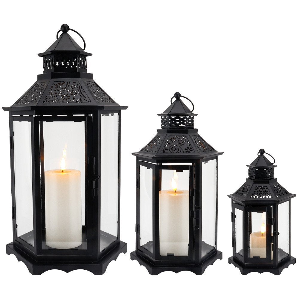 Three black metal and glass lanterns of varying sizes, each holding a lit white pillar candle, on a white background.