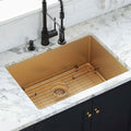 Gold stainless steel undermount kitchen sink with a grid drain and black faucet on a marble countertop.