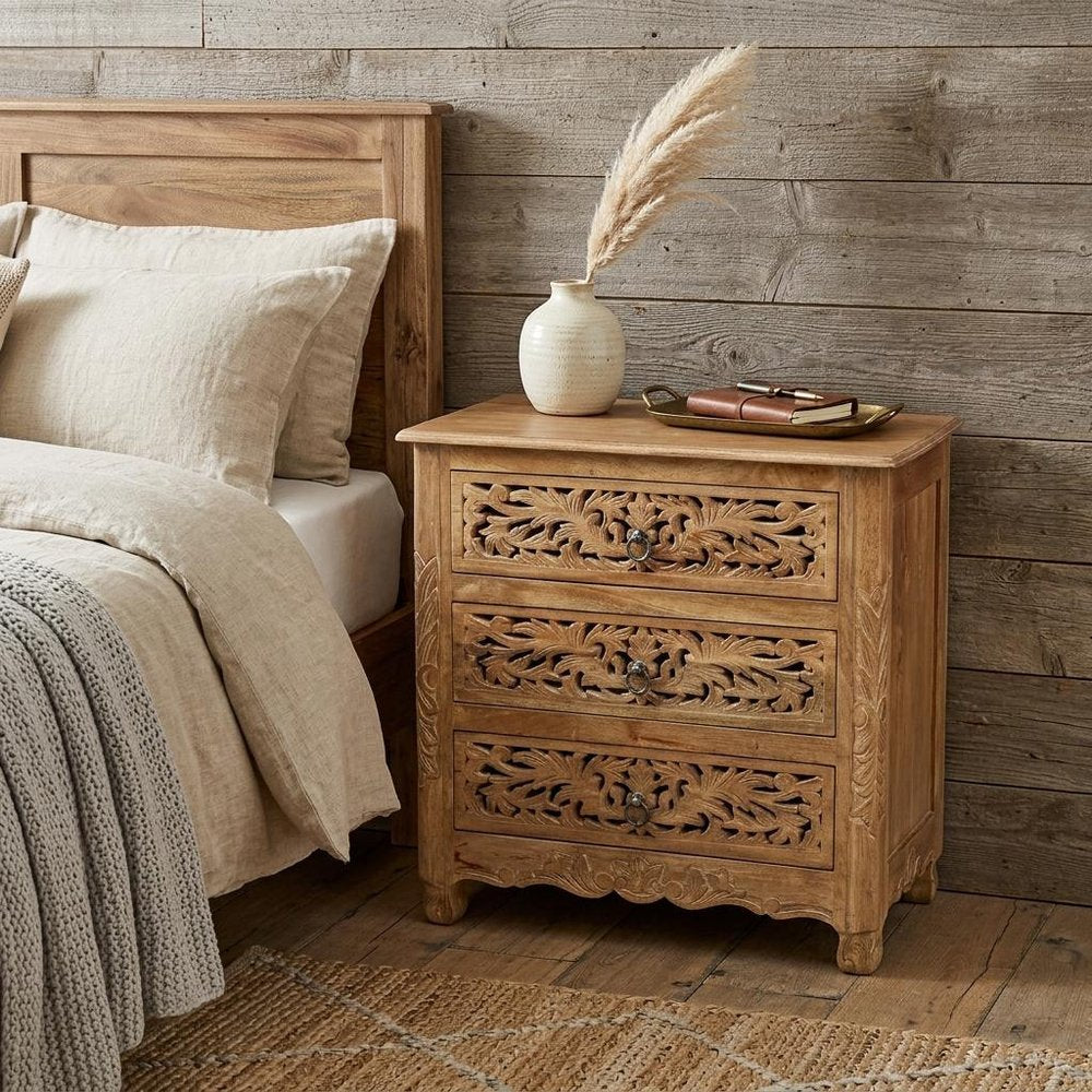 30" Brown Solid Wood Square Distressed Carved Floral Three Drawer Nightstand styled in a furnished interior with a tan wall on a dark wood floor.