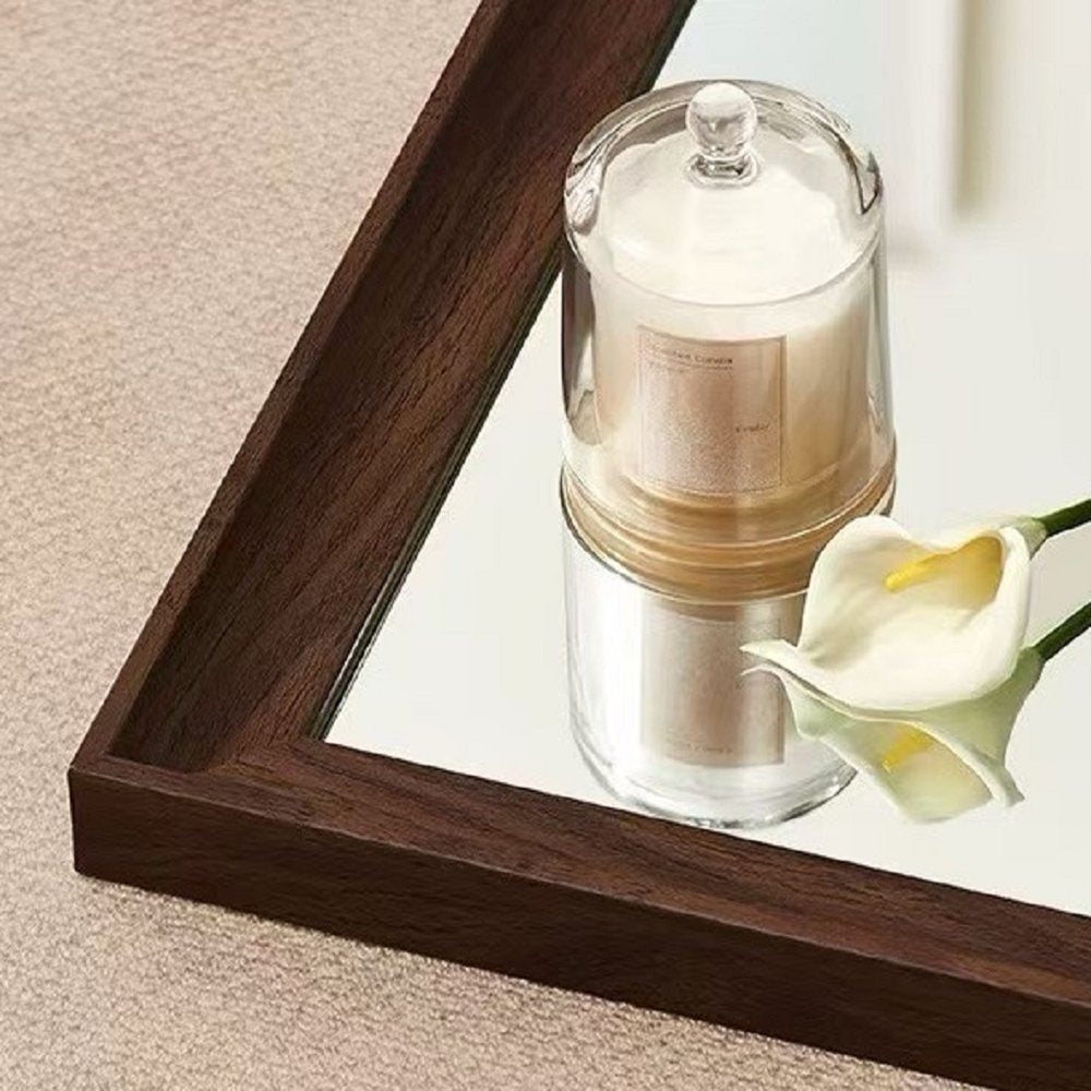 Brown wood framed mirror with a candle and white calla lily on a reflective surface.