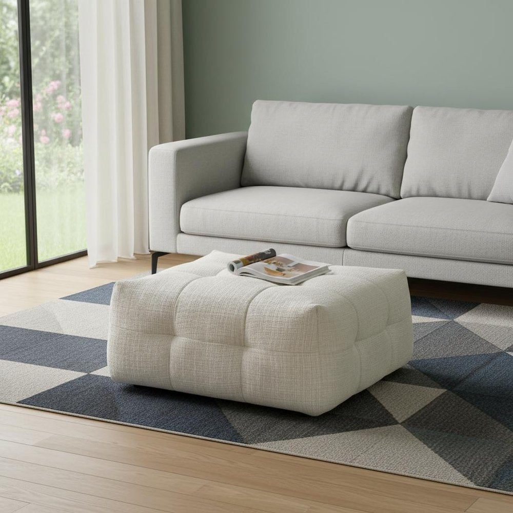 36" Beige and Black Chenille Tufted Pouf Ottoman styled in a furnished interior with a gray wall on a wood floor.