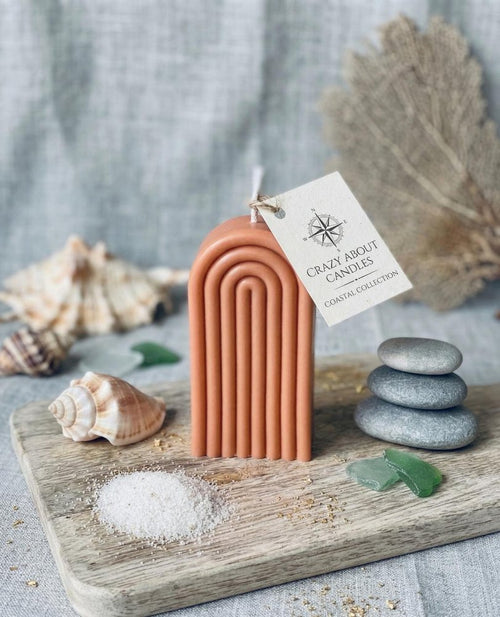 Terracotta arch candle with a tag reading "Crazy About Candles Coastal Collection" on a wooden board with shells and sea glass.