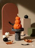 3" Orange Pumpkin And Apple Scented Dimensional Pumpkin Trio Soy Wax Candle displayed on a wood tabletop in a furnished interior against a dark brown wall.